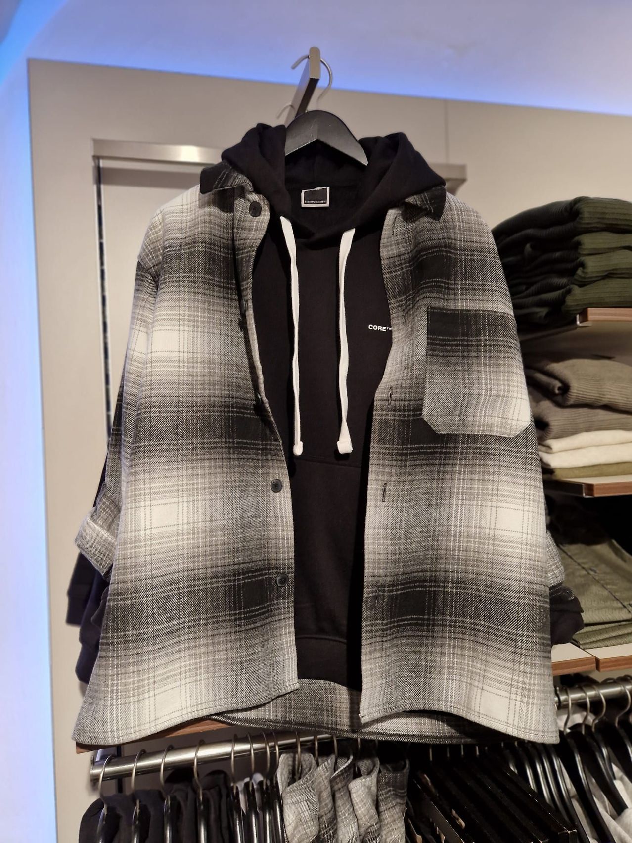 Eine schwarz-weiß karierte Jacke mit Kapuze und Knöpfen wird in einem Bekleidungsgeschäft an einem Kleiderbügel ausgestellt.