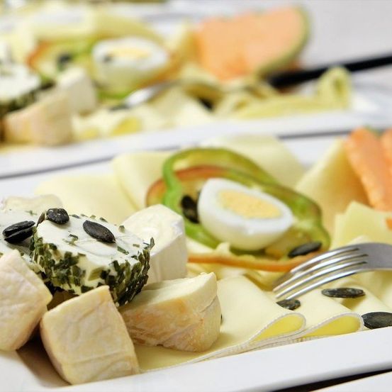 Ein weißer Teller mit verschiedenen Käsesorten, einschließlich eines runden Käses mit Mohnsamen und Scheiben gekochten Eies.