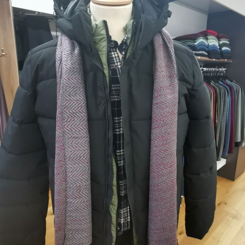 Ein Dummy zeigt eine schwarze Daunenjacke mit einem gemusterten Schal, einem grünen Hemd und einem karierten Hemd in einem Bekleidungsgeschäft.