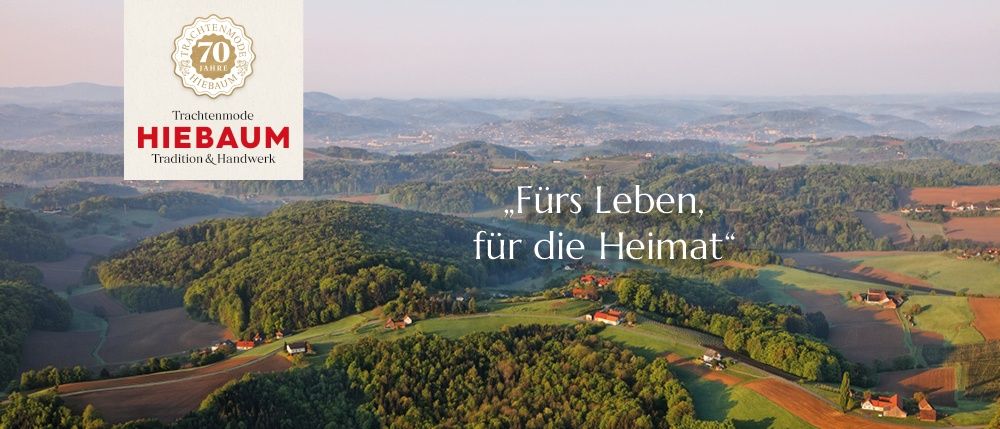 Luftaufnahme einer ländlichen Landschaft mit grünen Feldern, Bäumen und Häusern. Das Bild zeigt ein Logo für 'HIENBAUM' mit dem Slogan 'Fürs Leben, für die Heimat'. Im Hintergrund sind Berge zu sehen.