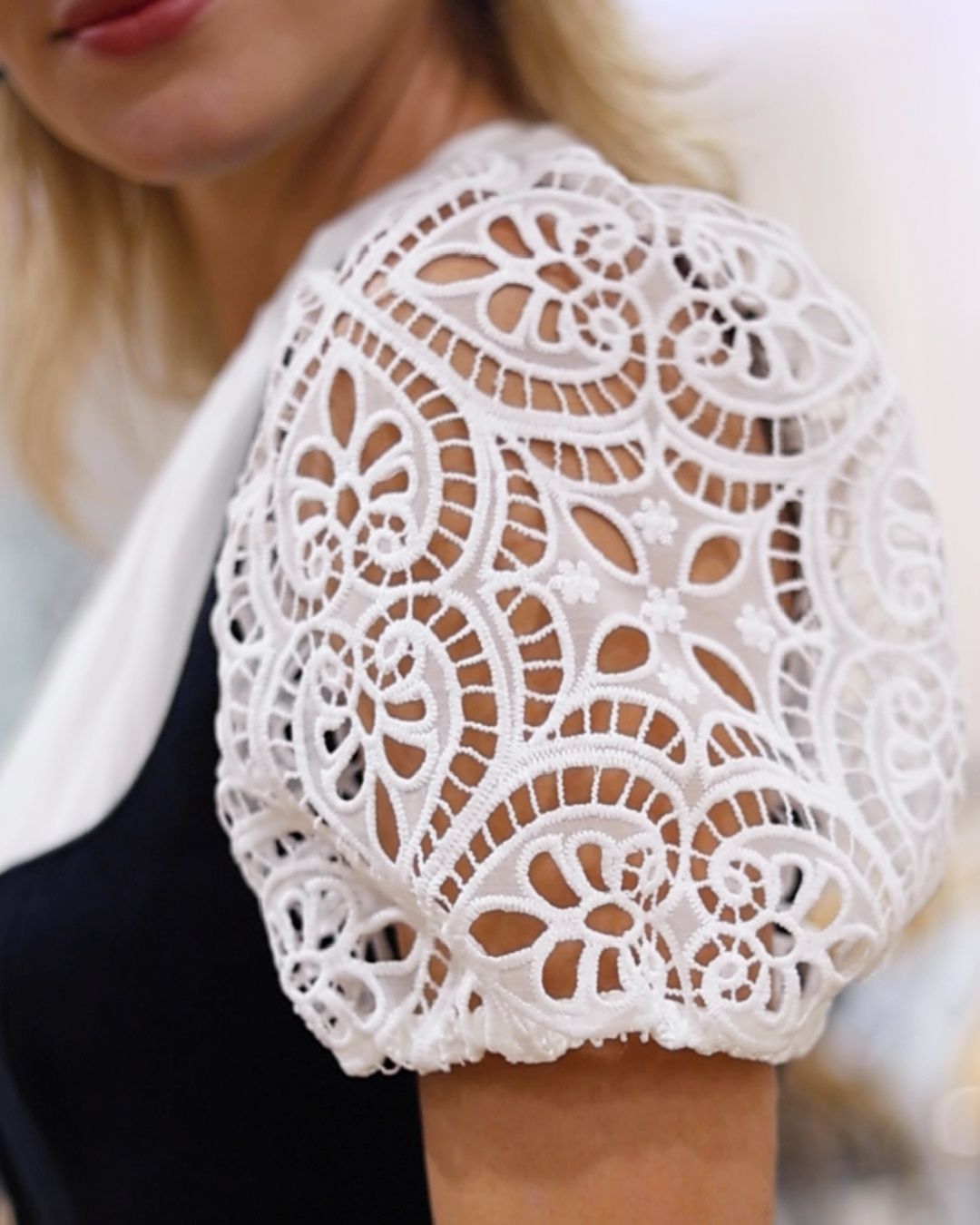 Ein Nahaufnahme der Schulter einer Frau mit einer weißen Spitzenüberlagerung mit Blumenmustern. Die Spitze ist filigran mit detaillierten Designs.