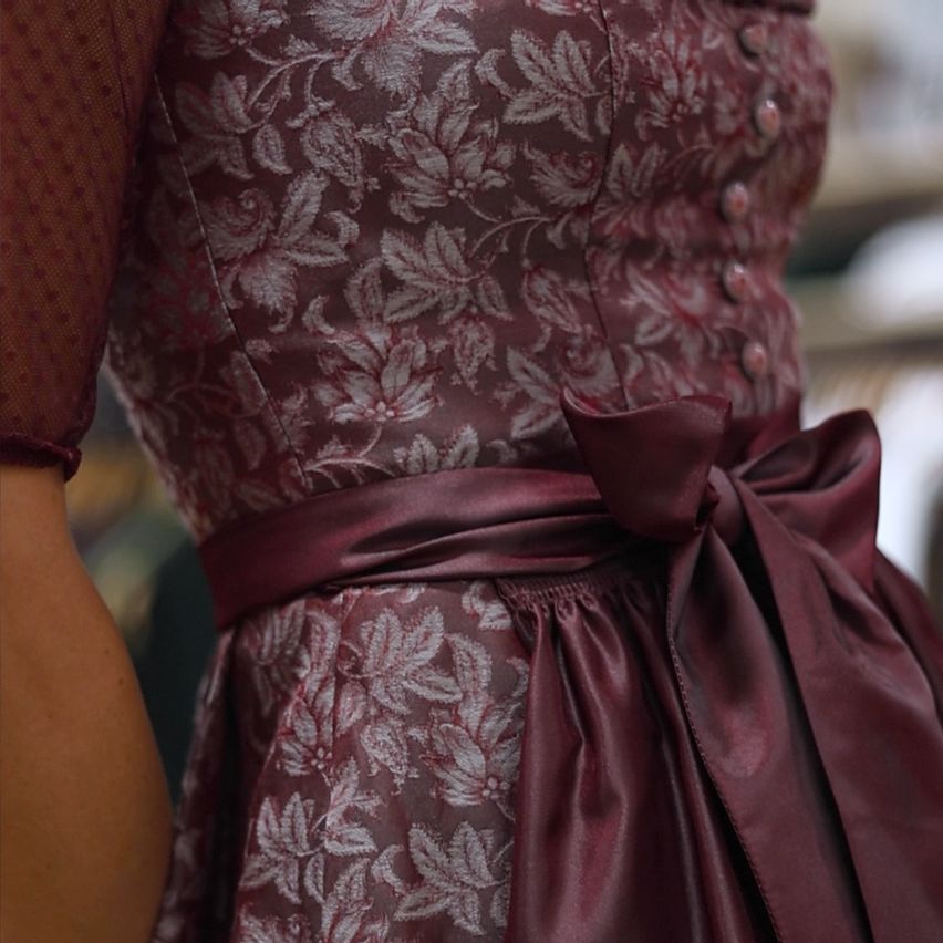 Eine Nahaufnahme eines weinroten Blumenkleides mit einer Schleife an der Taille und Knöpfen auf der Vorderseite.