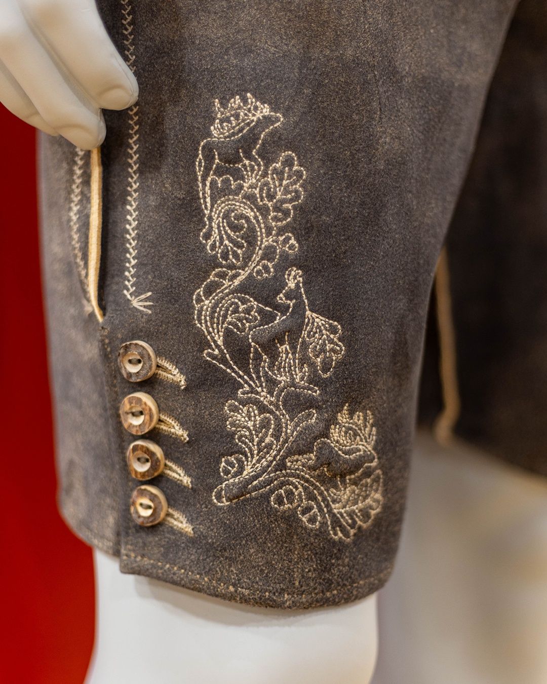 Nahaufnahme einer Hose mit aufwendigen Blumendesigns und Goldfäden, die auf einem Mannequin mit einer behandschuhten Hand ausgestellt wird.