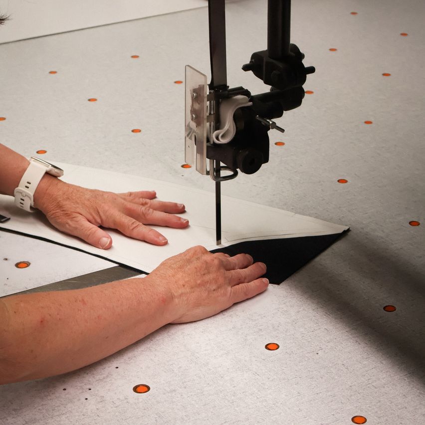 A person is using a band saw to cut a piece of paper on a table with orange dots.