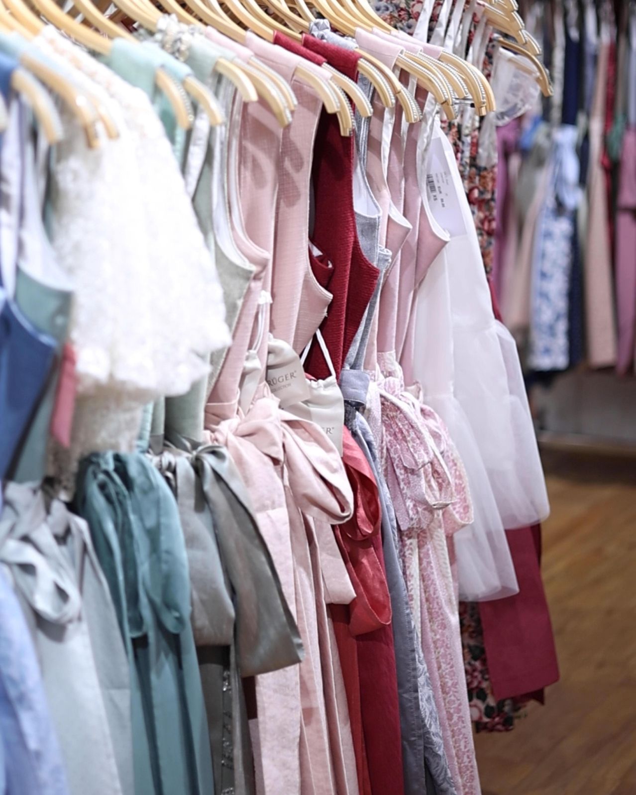 A row of dresses in various colors and styles is hanging on wooden hangers in a store.