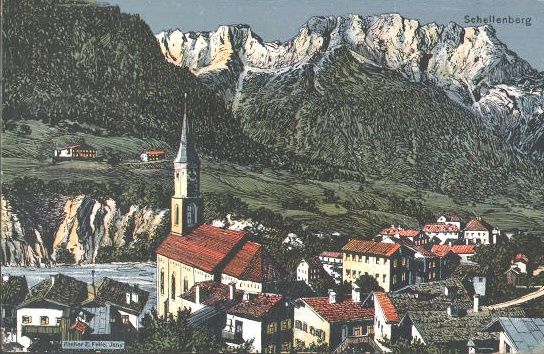 Eine Luftaufnahme eines Dorfes mit rot gedeckten Häusern und einem Kirchturm. Das Dorf ist von üppigen grünen Hügeln und Bergen in der Ferne umgeben.
