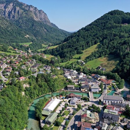 Eine Luftaufnahme eines Dorfes, umgeben von Bergen und Bäumen. Das Dorf liegt in der Nähe eines Flusses und hat Gebäude verschiedener Größen und Farben.
