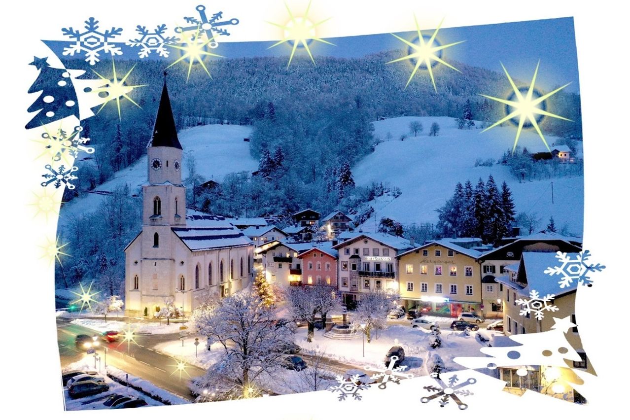 Eine Winterlandschaft zeigt eine verschneite Stadt mit Gebäuden, einer Kirche und einem Berg im Hintergrund. Schneeflocken und Sterne schmücken die Szene.