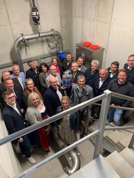 Eine Gruppe von Menschen, möglicherweise Mitarbeiter, posiert für ein Foto in einem Gebäude mit Industrieausrüstung. Sie stehen auf einer Treppe.