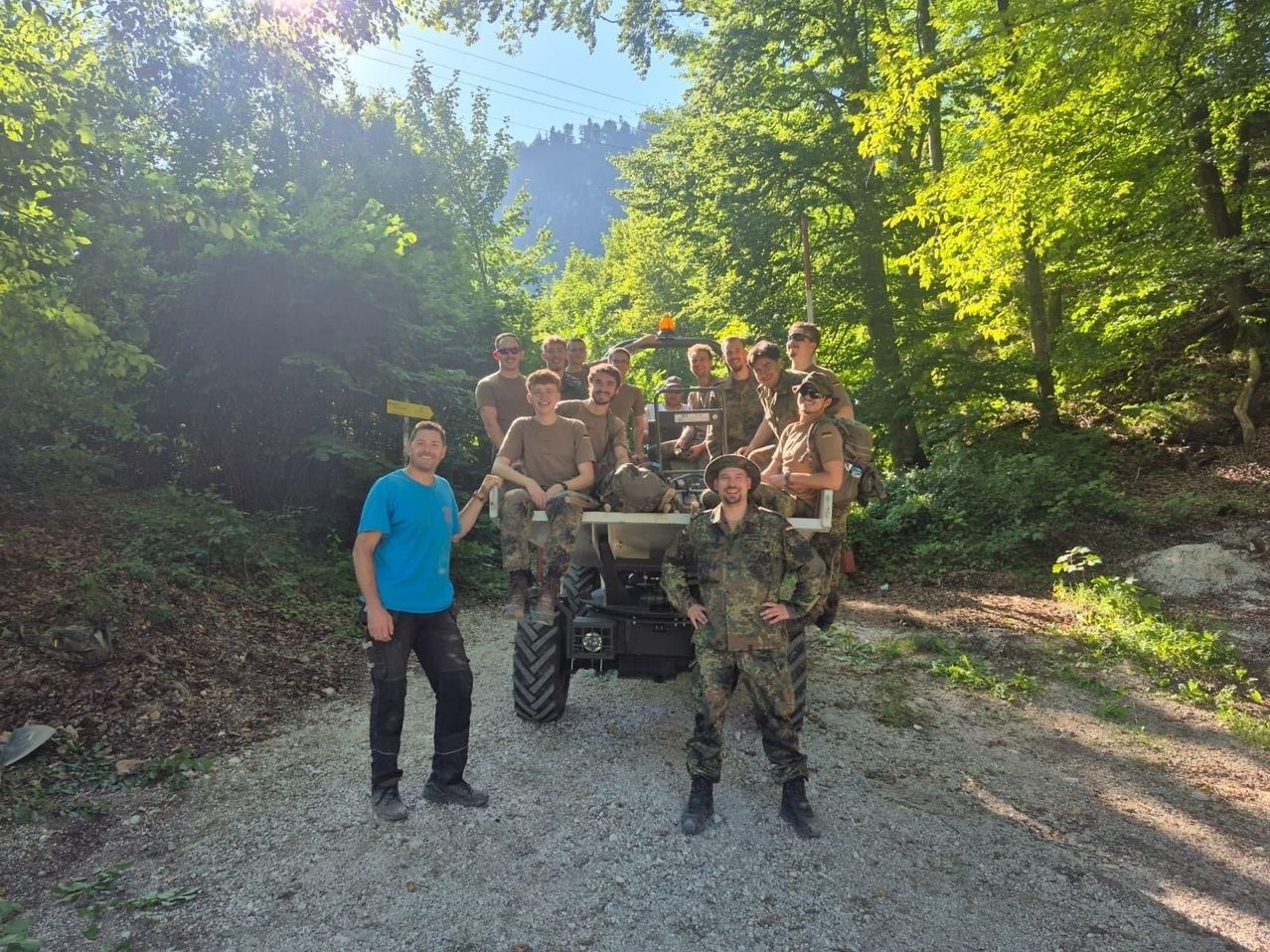 A group of soldiers in camouflage uniforms are posing for a photo in front of a vehicle in a forest.