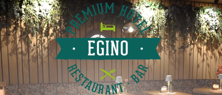 Innenansicht eines Premium-Hotels mit einem Restaurant und einer Bar namens Egino. Die Wände sind mit hängenden Pflanzen und Holzpaneelen geschmückt. Zwei Tische sind mit Lampen und Besteck gedeckt.