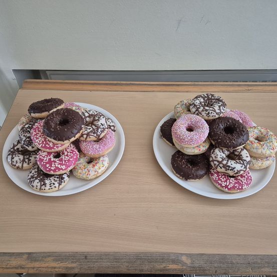 Zwei weiße Teller auf einem Tisch enthalten eine Auswahl an Schokoladen- und rosa glasierten Donuts mit Streuseln.