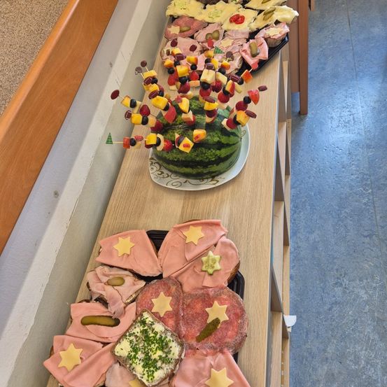 Ein hölzerner Tisch zeigt eine Vielzahl von Sandwiches, darunter eines mit einem Sterndesign darauf und einem Wassermelone auf einem Teller obenauf.