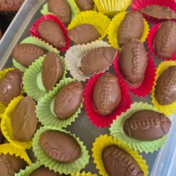 Ein Tablett gefüllt mit footballförmigen Schokoladen, jede in leuchtende Papierbecher eingewickelt. Die Schokoladen sind so gestaltet, dass sie Footballs mit detaillierten Designs ähneln.