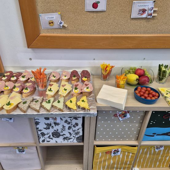 Ein Tisch mit verschiedenen Sandwiches, Obst und Gemüse. Der Tisch ist mit einer Silberfolie verziert. Unten stehen verschiedene Aufbewahrungsboxen.