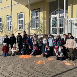 Eine Gruppe von Kindern in Winterkleidung posiert für ein Foto vor einem gelben Gebäude mit mehreren Fenstern und einer Metallbrüstung.
