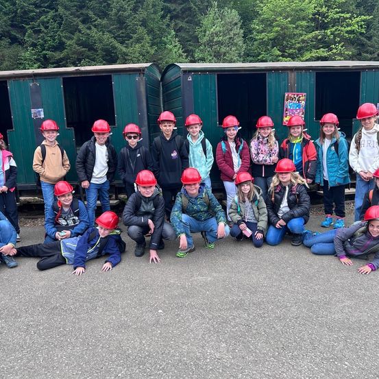 Eine Gruppe von Kindern in roten Helmen und Jacken posiert für ein Foto vor grünen Eisenbahnwaggons.