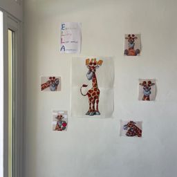 Eine weiße Wand mit mehreren Karikaturbildern von Giraffen und Text, darunter eines, das 'ELLA' und ein anderes, das 'EINFÜHLSAM' sagt.