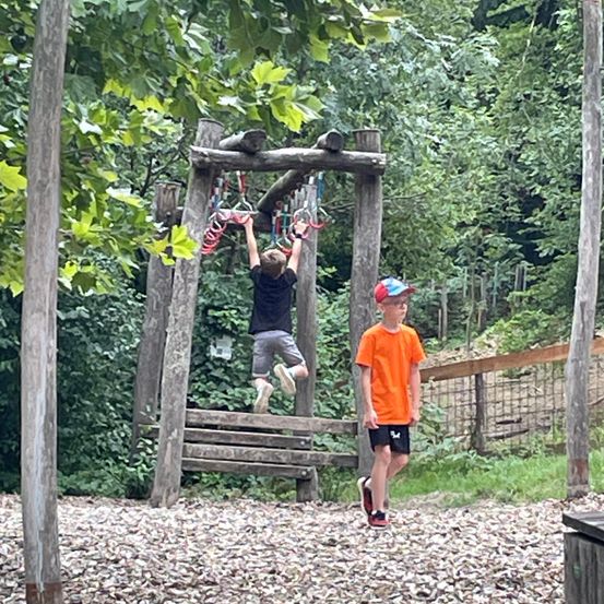Ein Junge klettert auf eine Holzstruktur in einem Park, während ein anderer Junge zusieht.