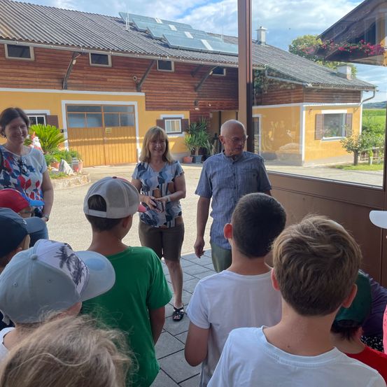 Eine Gruppe von Menschen, einschließlich Kindern, versammelt sich vor einem gelben Gebäude mit Solarpanelen auf dem Dach.