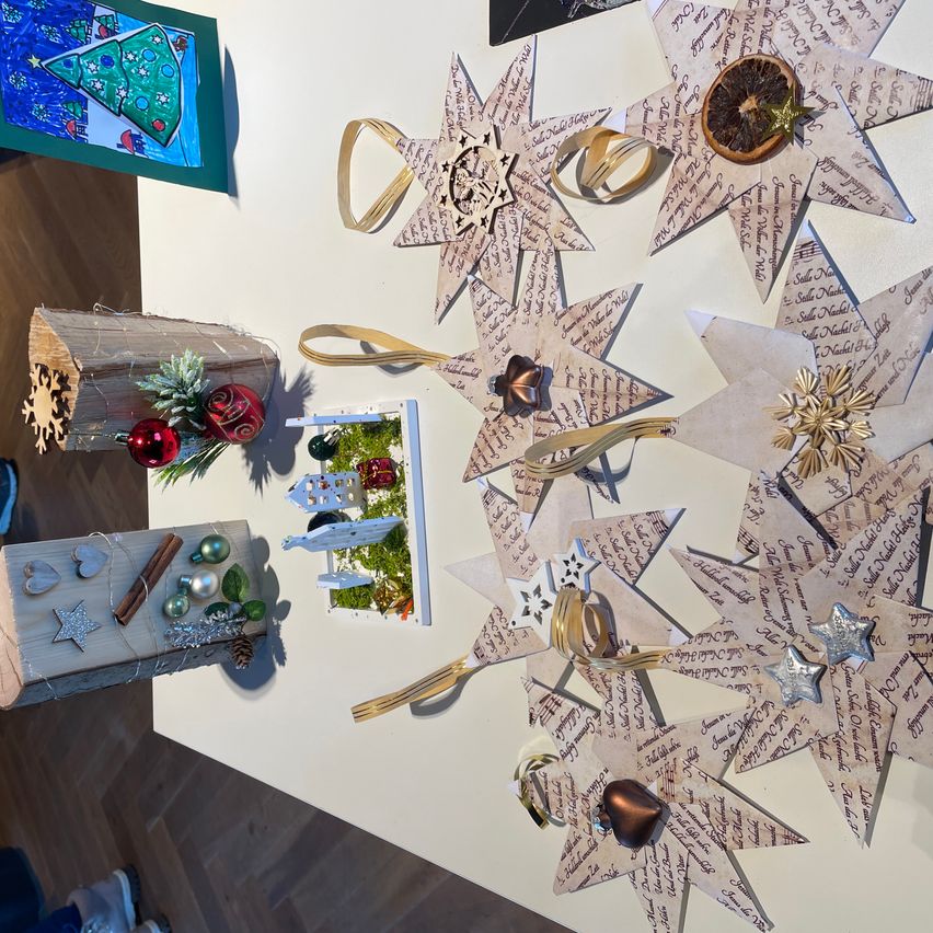 Ein Tisch mit Weihnachtsdekorationen, darunter Sternverzierungen, Bänder und Ornamente. Eine Holzkiste mit Sternen und Zimtstangen befindet sich links.