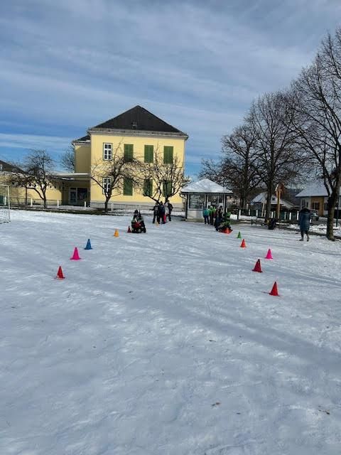 Ein verschneiter Platz mit Verkehrskegeln und Menschen in der Nähe eines Gebäudes mit grünen Fensterläden.