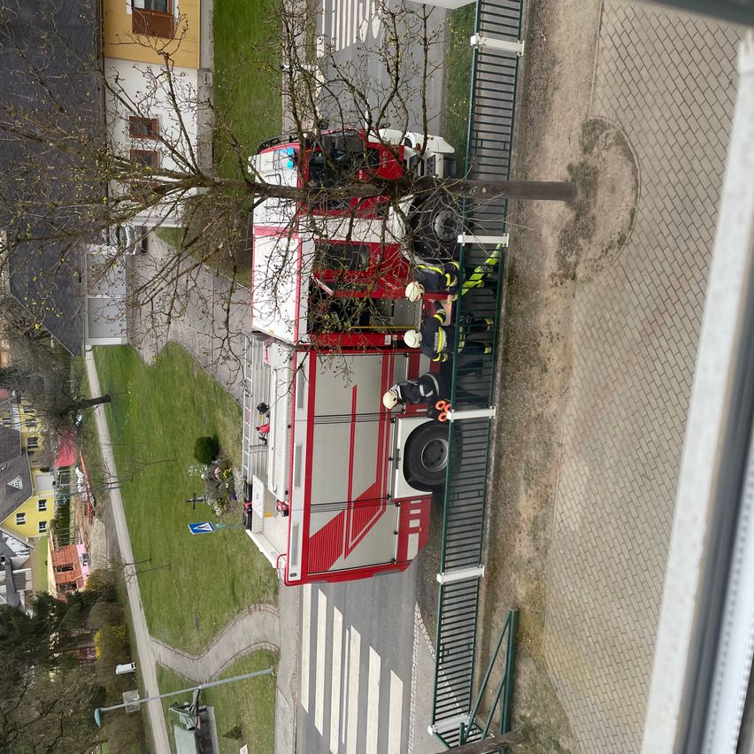 Ein roter und weißer Feuerwehrwagen ist am Straßenrand geparkt, an dem Feuerwehrleute arbeiten.