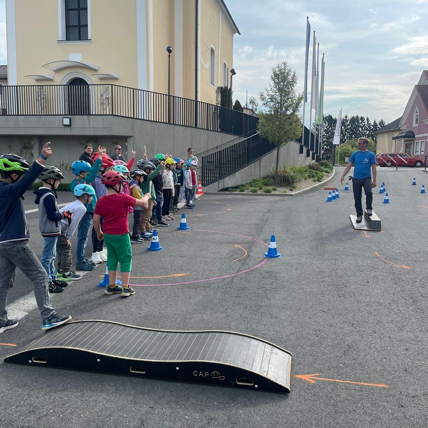 Eine Gruppe von Kindern in Helmen steht hinter einer Rampe mit Hütchen und einem Mann, der auf einem Skateboard auf einer Rampe geht.