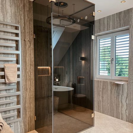 Ein modernes Badezimmer mit einer Glasdusche, Marmorwänden, einer weißen Badewanne und einem Holzhocker. Ein Handtuch hängt an einem Handtuchhalter.