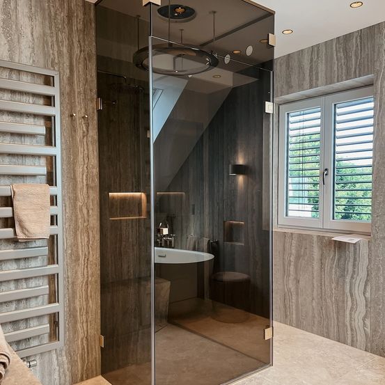 Ein modernes Badezimmer mit einer Glasdusche, Marmorwänden, einer weißen Badewanne und einem Holzhocker. Ein Handtuch hängt an einem Handtuchhalter.