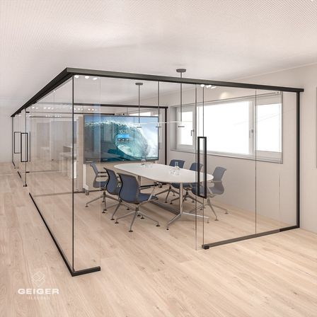 Ein Besprechungsraum mit einer Glaswand und einem großen Monitor, der eine Welle zeigt. Ein runder weißer Tisch mit blauen Stühlen umgibt ihn. Der Raum hat einen Holzboden und weiße Wände.