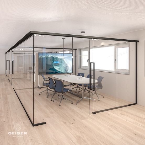 Ein Besprechungsraum mit einer Glaswand und einem großen Monitor, der eine Welle zeigt. Ein runder weißer Tisch mit blauen Stühlen umgibt ihn. Der Raum hat einen Holzboden und weiße Wände.