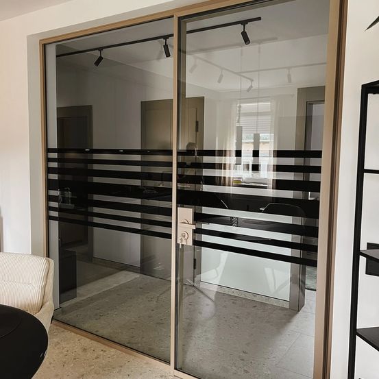 Ein Bild eines modernen Innenraums mit einer Glastrennwand mit schwarzen und weißen Streifen, dem Spiegelbild einer Person und einem Metallgriff.