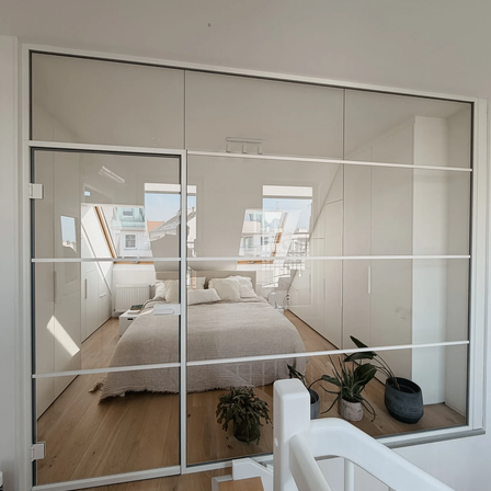 Ein Zimmer mit weißen Wänden, einer Glastür, einem Bett und einigen Pflanzen. Der Raum hat ein modernes und minimalistisches Design.