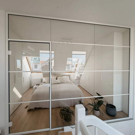Ein Zimmer mit weißen Wänden, einer Glastür, einem Bett und einigen Pflanzen. Der Raum hat ein modernes und minimalistisches Design.