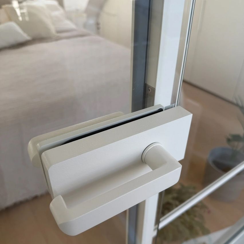 Eine Nahaufnahme eines weißen Schiebetürgriffs aus Glas mit einem unscharfen Hintergrund eines Schlafzimmers mit einem Bett und einer Topfpflanze.