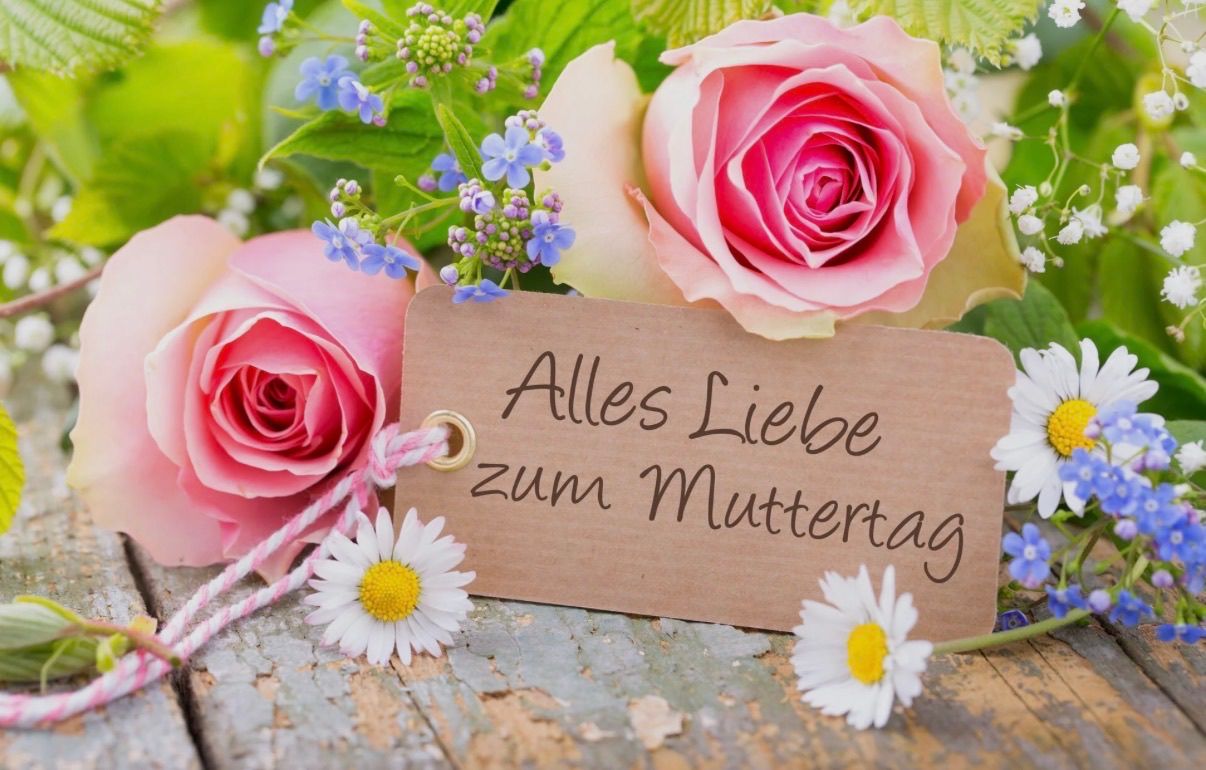 Ein brauner Anhänger mit den Worten 'Alles Liebe zum Muttertag' ist an einem Strauß rosa Rosen und Gänseblümchen auf einer Holzoberfläche befestigt.