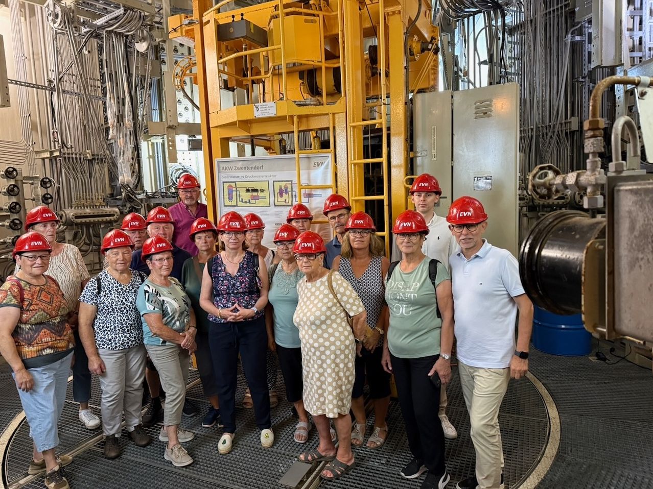 Eine Gruppe von Menschen in Schutzhelmen posiert für ein Foto vor einer großen gelben Maschine.