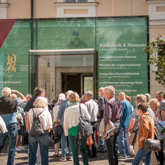 Eine Menschenmenge steht vor dem Eingang der Bibliothek & Museum, einem gläsernen Gebäude mit einem grünen Schild.