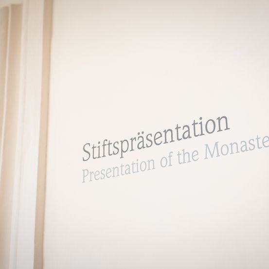 Eine weiße Wand mit dem Text 'Stiftungsprasentation Presentation of the Monastery' in schwarzem Text.