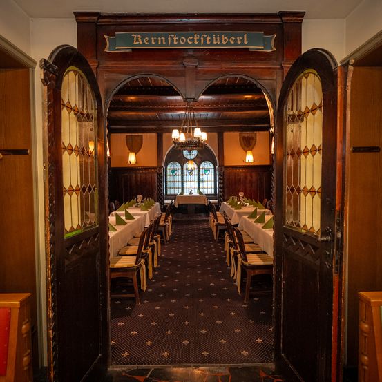 Ein Innenansicht eines Restaurants mit Holztüren, einer Kronleuchter und mehreren Tischen für das Essen. Das Schild heißt Bernstofftuber.