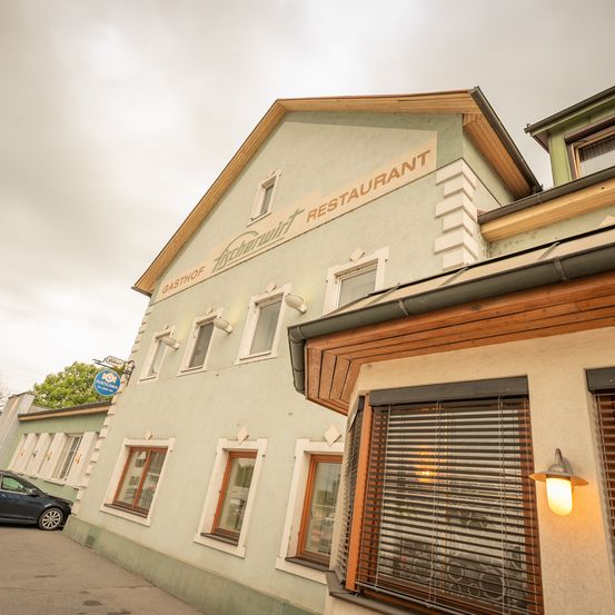 Ein Gebäude mit dem Schild 'Zirchowwirt Gasthof Restaurant' steht an einer Straße. Das Gebäude hat eine graue Außenseite mit weißen Akzenten. Ein Auto ist auf der linken Seite geparkt.