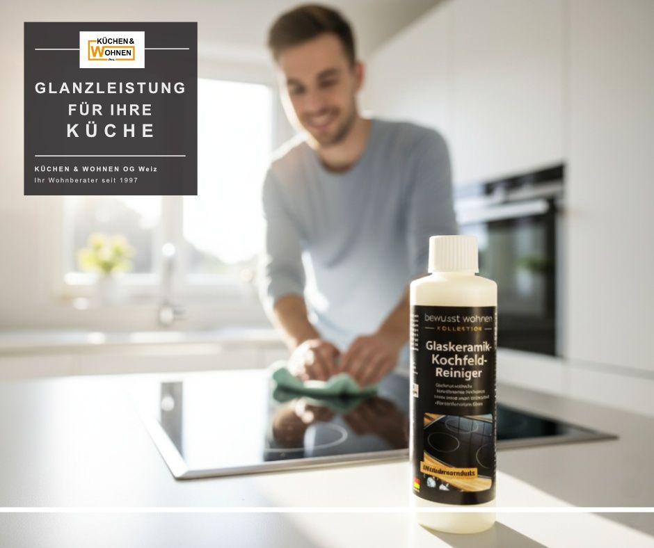 Ein Mann reinigt eine Küchentheke mit einer Flasche Glaskeramik-Kochfeldreiniger vor ihm. Er lächelt. Es gibt eine Reflexion des Mannes auf dem Glaskochfeld.