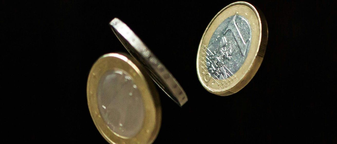 Vier Münzen befinden sich in der Luft, vor einem schwarzen Hintergrund. Sie sind gold und silber in der Farbe, mit komplizierten Designs.