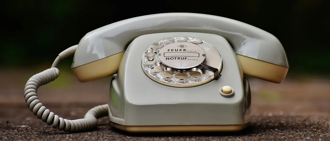 Ein altes weißes Wählscheibentelefon mit den Worten 'FEUER' und 'NOTRUF' darauf liegt auf dem Boden.