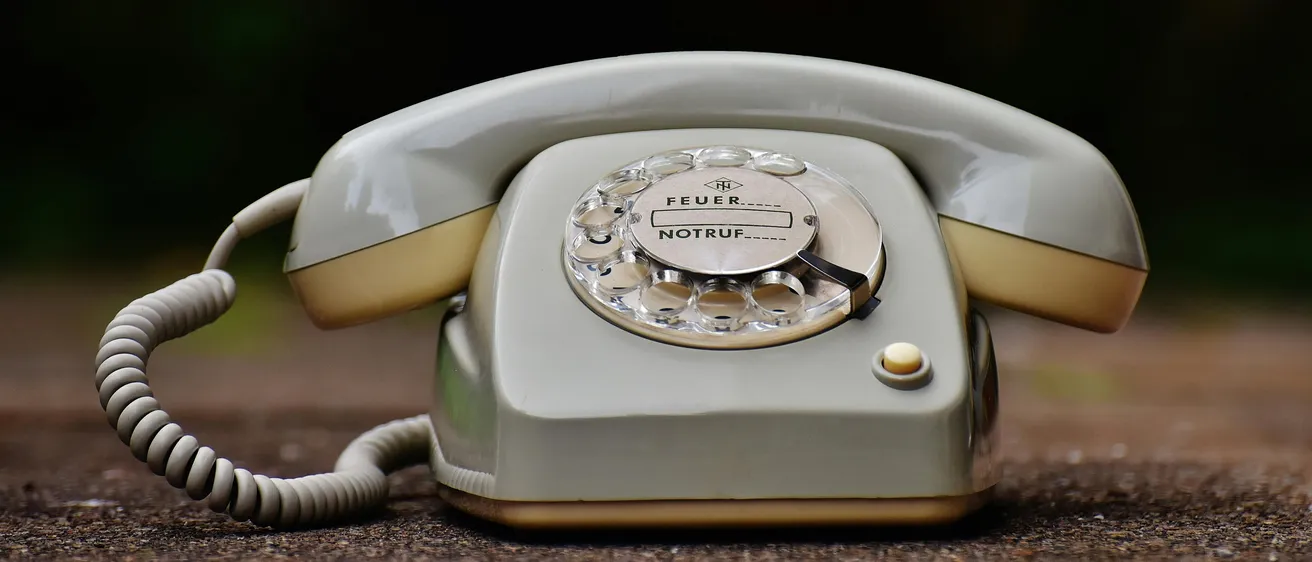 Ein altes weißes Wählscheibentelefon mit den Worten 'FEUER' und 'NOTRUF' darauf liegt auf dem Boden.