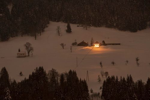 Eine schneebedeckte Landschaft mit mehreren Häusern, einem hellen gelben Schild und Bäumen im Hintergrund.