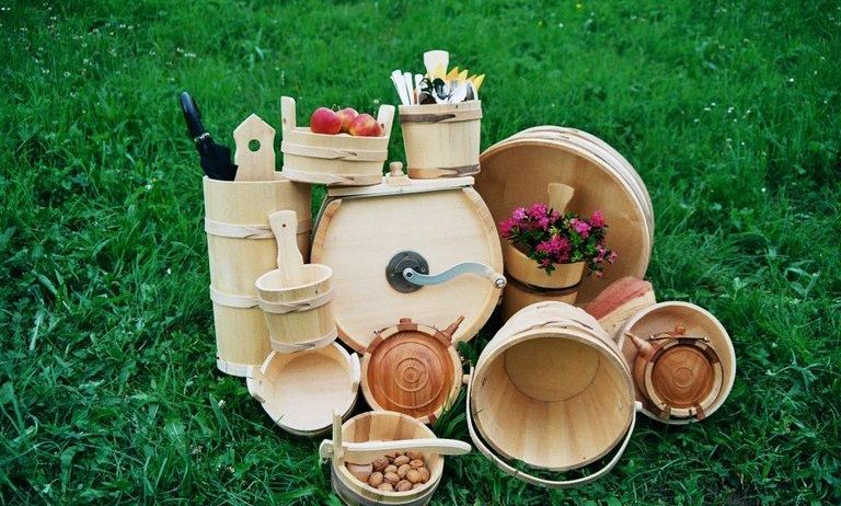 Eine Sammlung von Holzeimern, Schüsseln und einem Fass auf einem Grasfeld. Einige Eimer enthalten Früchte, Blumen und Utensilien.