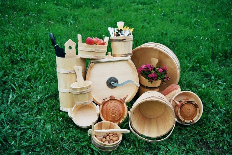 Eine Sammlung von Holzeimern, Schüsseln und einem Fass auf einem Grasfeld. Einige Eimer enthalten Früchte, Blumen und Utensilien.