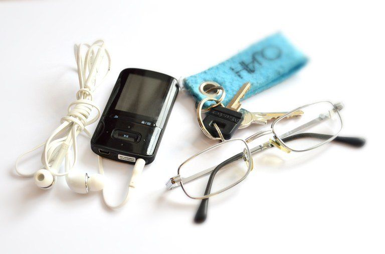 Ein schwarzer MP3-Player mit Kopfhörern, eine Brille und ein Schlüsselanhänger liegen auf einer weißen Oberfläche.